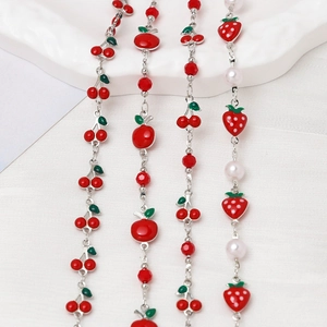 Detailed view of red enamel fruit charms and beads on silver chains for jewelry making
