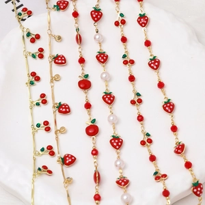 Close-up of gold chain jewelry with red enamel fruit charms and pearls in a ceramic tray