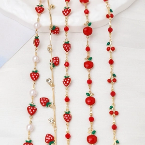 Macro shot of gold-plated chains featuring red enamel fruit charms and faux pearls