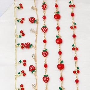 Detail of gold chains featuring red enamel fruit charms and sparkly rhinestones