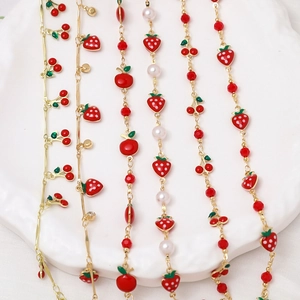 Detail of gold chain necklaces with red cherry, strawberry charms and faux pearls