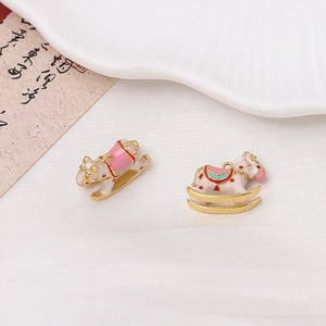 Detailed macro of gold plated enamel rocking horse charms on white silk fabric