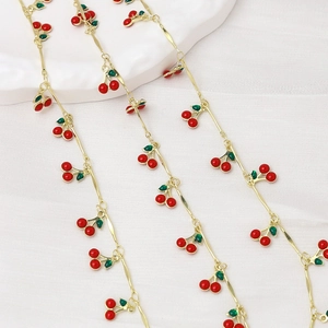 Close-up of gold chain with glossy red cherry pendants for DIY jewelry making
