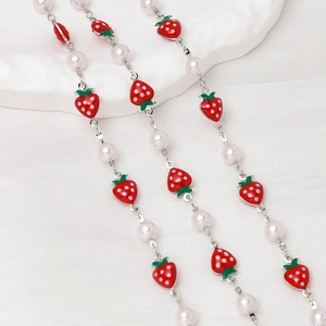 Detail of beaded necklace with white pearls and vibrant red oil-dripped strawberry charms