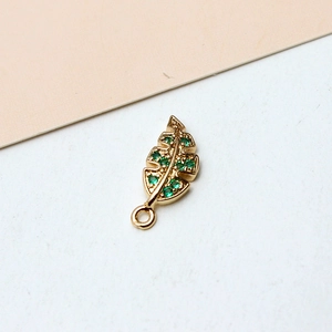 Macro view of gold-plated leaf pendant with green zircon stones and open ring detail