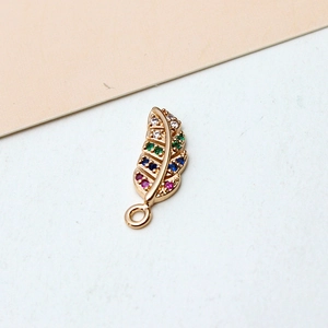 Macro detail of a gold feather pendant with colorful pavé zircons and a closed ring connector