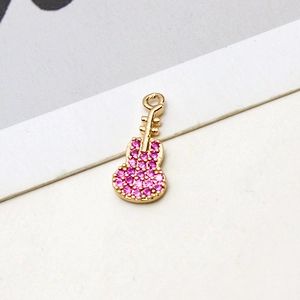 Detalle macro de un colgante de guitarra dorado con circonitas rosas para joyas DIY