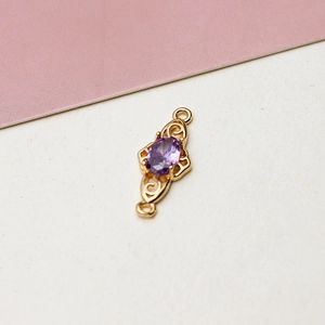 Macro detail of gold-plated pendant connector with oval purple zircon and filigree pattern