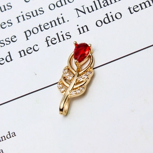 Macro view of a gold feather pendant with a red teardrop stone and white zircons