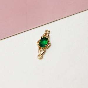 Close-up of gold-plated pendant with green oval gemstone and hollow scrollwork for DIY