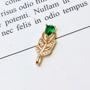Macro view of gold feather pendant with pear-shaped green gem and micro-set cubic zirconia