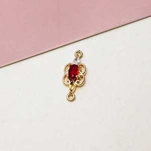 Detail of gold-plated jewelry connector with red gemstone and hollow floral pattern