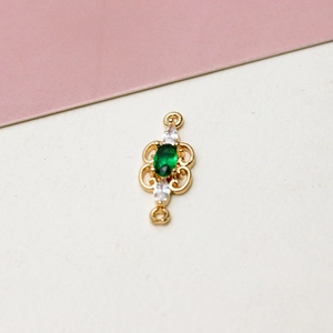 Detail view of a gold-plated connector with green oval gemstone and white cubic zirconia