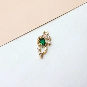 Macro detail of a gold dolphin pendant with emerald green stone and zircon micro-paving