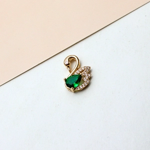 Close-up of gold-plated swan pendant with green pear-cut gemstone and white zircon accents