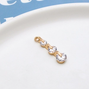 Detailed close-up of a three-stone gold pendant with clear round zircon in a ceramic dish