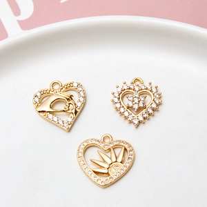 Macro view of gold-plated heart charms with zircons and hand, flower, and sun motifs