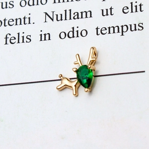 Macro shot of gold deer pendant with a green teardrop-shaped gemstone on white paper