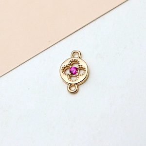 Macro detail of gold plated clover charm connector with a pink zircon stone inlay