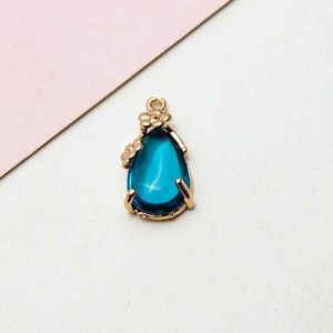 Macro shot of blue crystal water drop pendant with gold floral rim and hanging loop