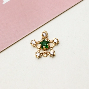 Dettaglio di un ciondolo a stella dorato con pietra verde e accenti in zirconi bianchi