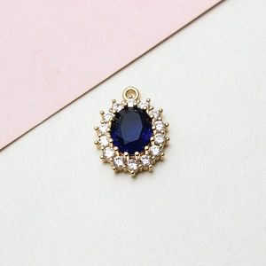 Close-up of oval gold pendant with blue gemstone and sparkling white zircon halo