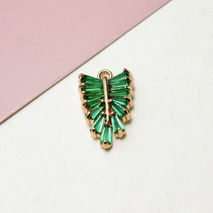 Macro detail of leaf-shaped gold pendant with emerald green cubic zirconia stones