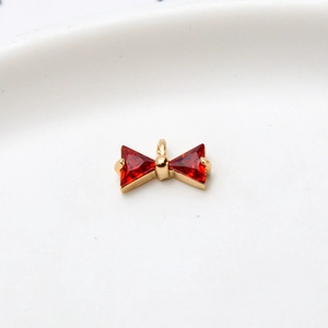 Macro detail of a golden bow pendant with red triangular zircons for DIY jewelry making