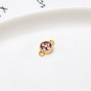 Macro detail of gold-plated flower charm with purple zircon and dual link loops