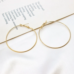 Detailed view of large gold-plated hoop earrings on a minimalist white textured backdrop