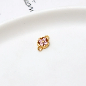 Macro detail of gold-plated flower connector charm with pink zircon and milgrain edges
