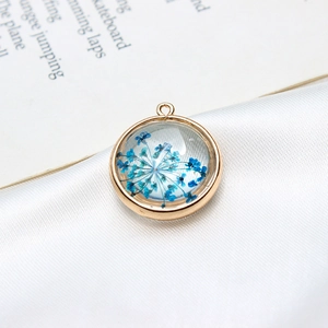 Détail macro d'un pendentif rond doré avec fleurs séchées bleues pour création de bijoux