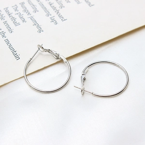 Macro shot of silver metal hoop earrings with pin closure on a white textured background
