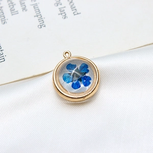 Vue macro détaillée d'un pendentif rond doré contenant une véritable fleur séchée bleue
