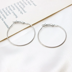 Macro detail of glossy silver geometric hoop earrings with clasp on white satin fabric