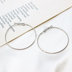 Macro detail of large polished silver-tone circular hoop earrings on white fabric