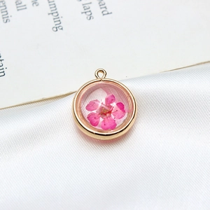Détail macro d'un pendentif rond plaqué or avec une vraie fleur séchée rose pour bijoux DIY