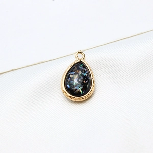 Macro detail of gold-plated teardrop pendant with iridescent resin and ripple edge frame