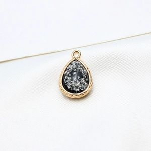 Macro view of water-drop resin pendant with gold plated edge and silver foil accents