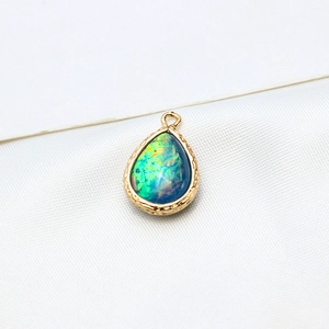 Macro shot of gold-plated teardrop opal pendant with detailed woven texture on silk