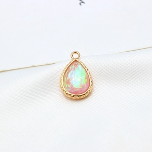 Macro detail of a gold-plated teardrop pendant with iridescent pink faux opal stone inlay