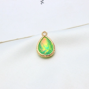 Detail of a gold-plated teardrop pendant with green resin opal inlay on white silk fabric