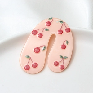 Close-up of pink acrylic U-shaped earrings with cherry patterns on a white ceramic plate