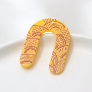 Macro detail of yellow acrylic arch earring with vintage etched fan patterns and hole