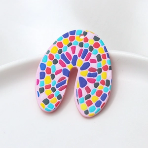 Macro detail of U-shaped acrylic earrings with colorful mosaic patterns on white ceramic tray