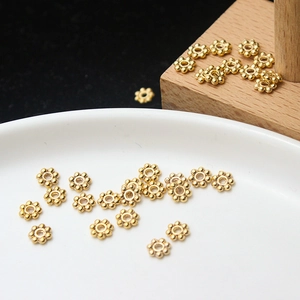 Gold-plated snowflake spacer beads for DIY jewelry making displayed on a white plate
