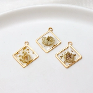 Detailed view of square gold-rimmed resin pendants with gold foil and dried flowers