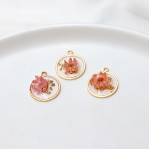 Macro detail of handmade resin floral pendants with pink dried flowers and gold leaf foil