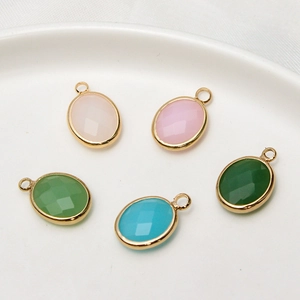 Oval faceted glass birthstone pendants in gold-plated settings on white ceramic