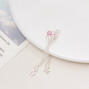 Dettaglio del ciondolo a fiocco argento con pietre rosa e nappe a stella su vassoio bianco